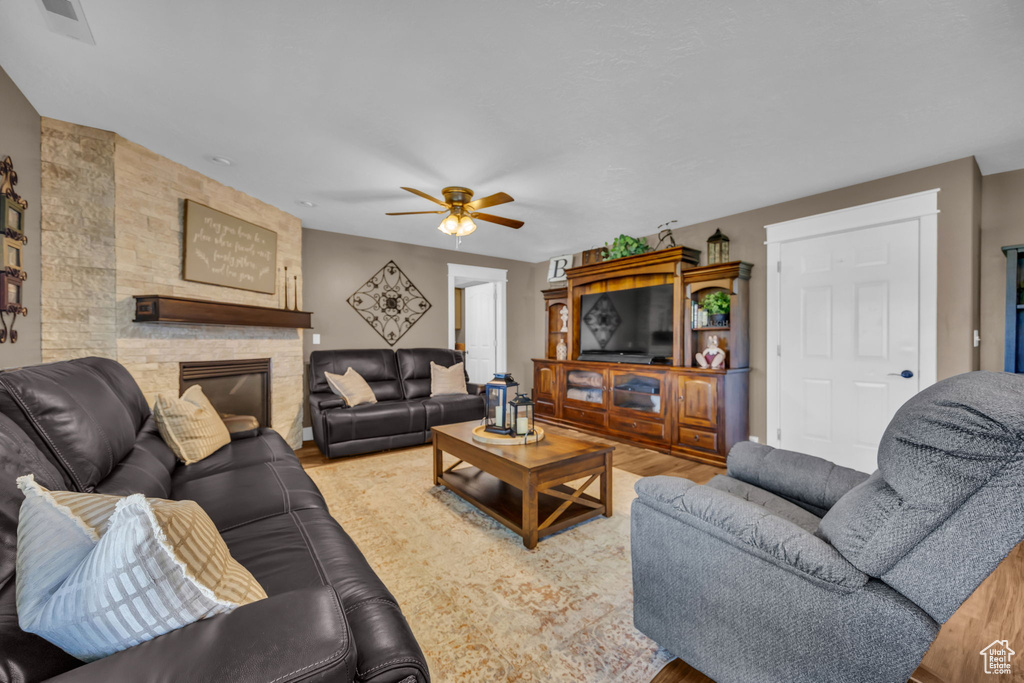 Living room featuring a ceiling fan, wood finished floors, and a stone fireplace