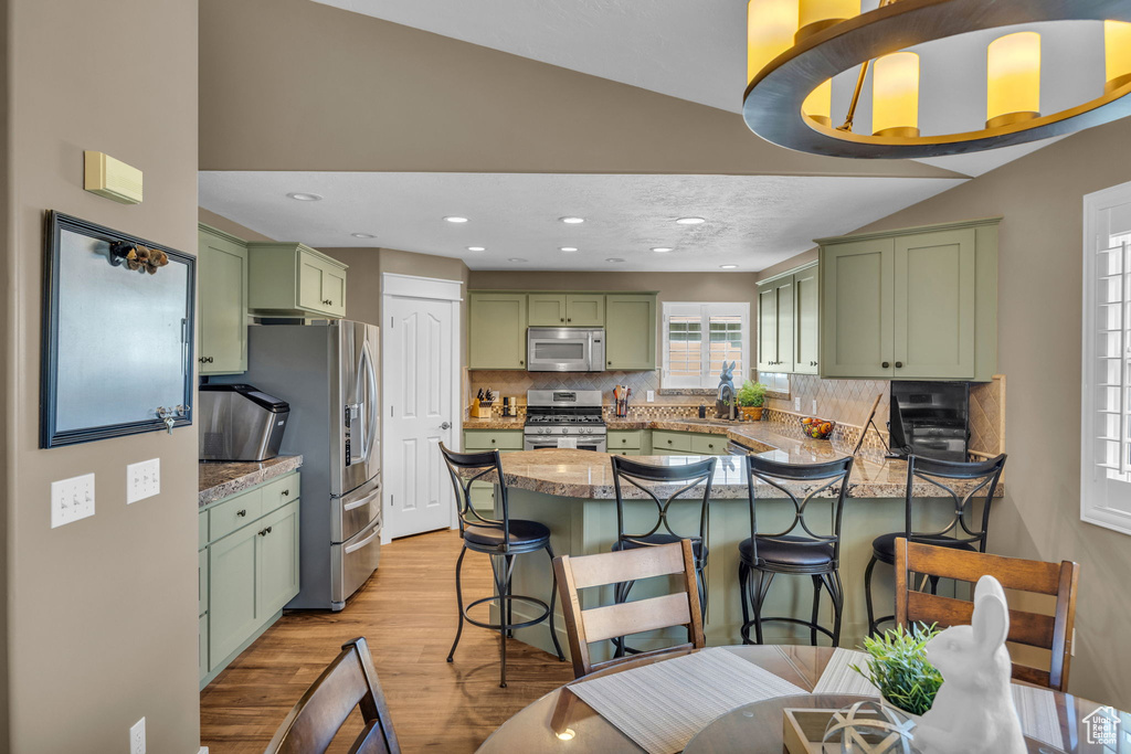 Kitchen with green cabinetry, stainless steel appliances, a peninsula, a kitchen breakfast bar, and recessed lighting