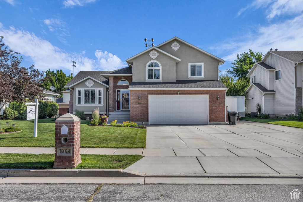 View of front of property featuring an attached garage, driveway, a front yard, stucco siding, and brick siding