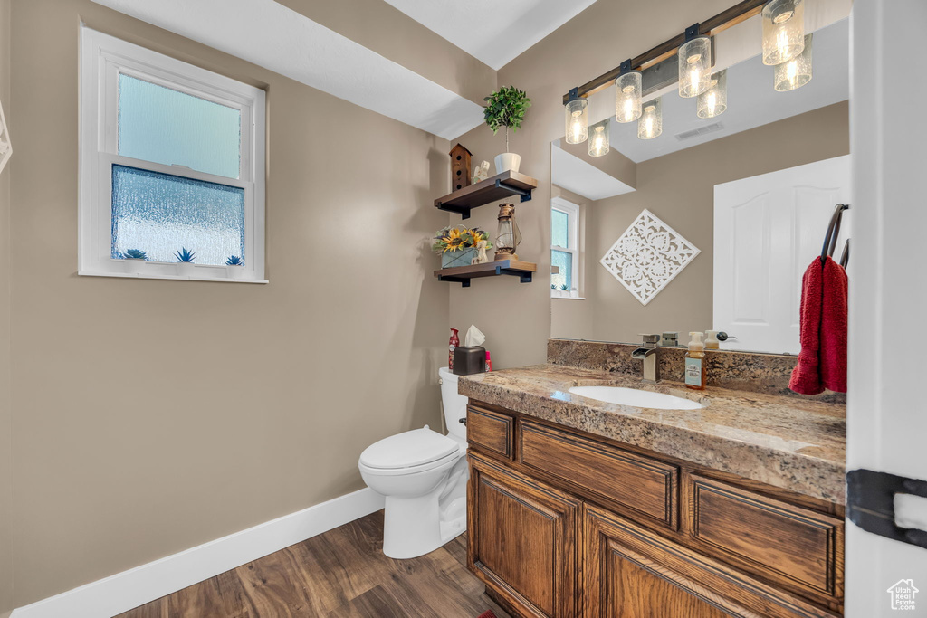 Half bathroom with baseboards, vanity, wood finished floors, and toilet