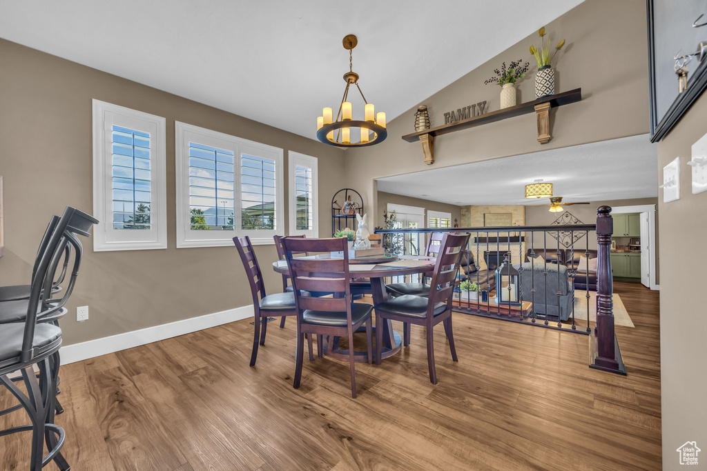 Dining space featuring a chandelier, wood finished floors, ceiling fan, baseboards, and lofted ceiling