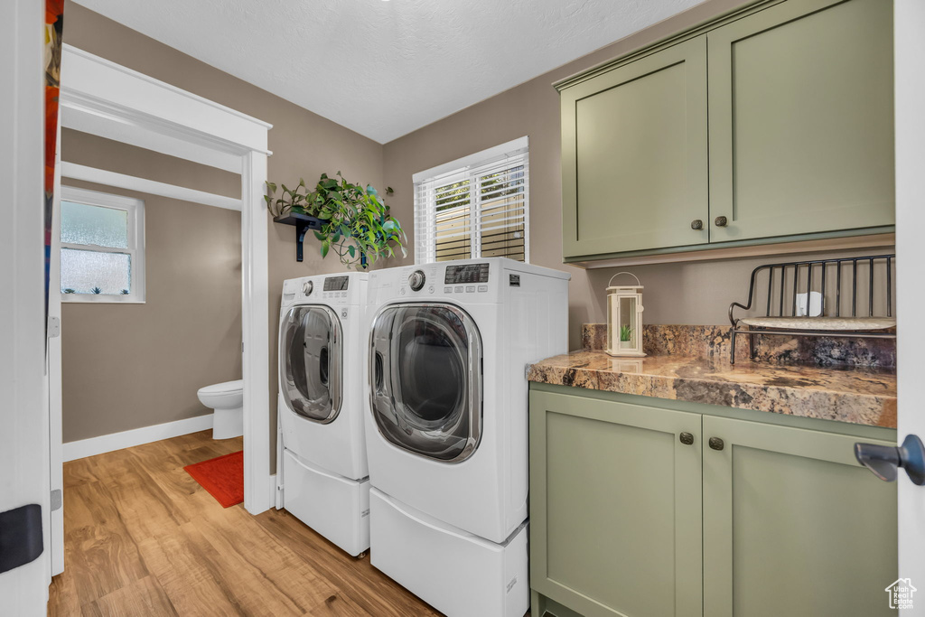 Laundry room featuring washing machine and clothes dryer, light wood-style floors, cabinet space, and plenty of natural light