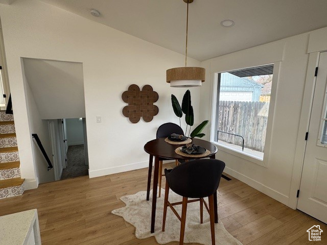 Dining room with lofted ceiling, light wood-style floors, baseboards, and stairway
