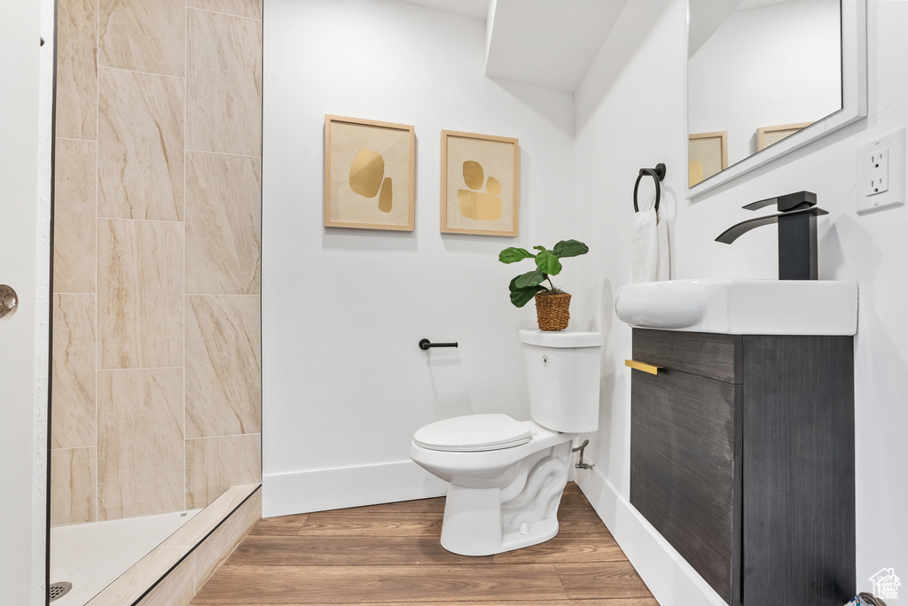 Bathroom featuring toilet, tiled shower, vanity, baseboards, and wood finished floors