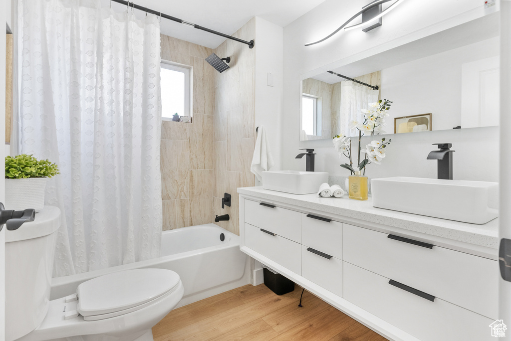 Full bath featuring toilet, shower / tub combo, double vanity, and wood finished floors