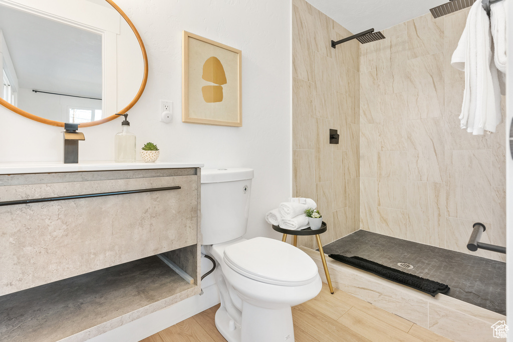Full bath featuring toilet, tiled shower, vanity, and wood finished floors
