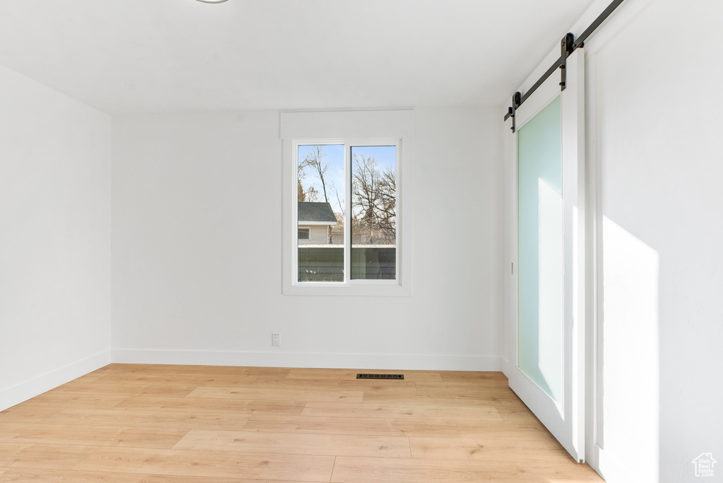 Spare room with a barn door, light wood-style floors, and baseboards