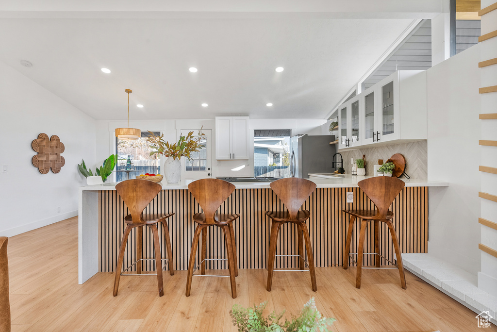 Kitchen featuring white cabinetry, a sink, light wood-style flooring, recessed lighting, and glass insert cabinets