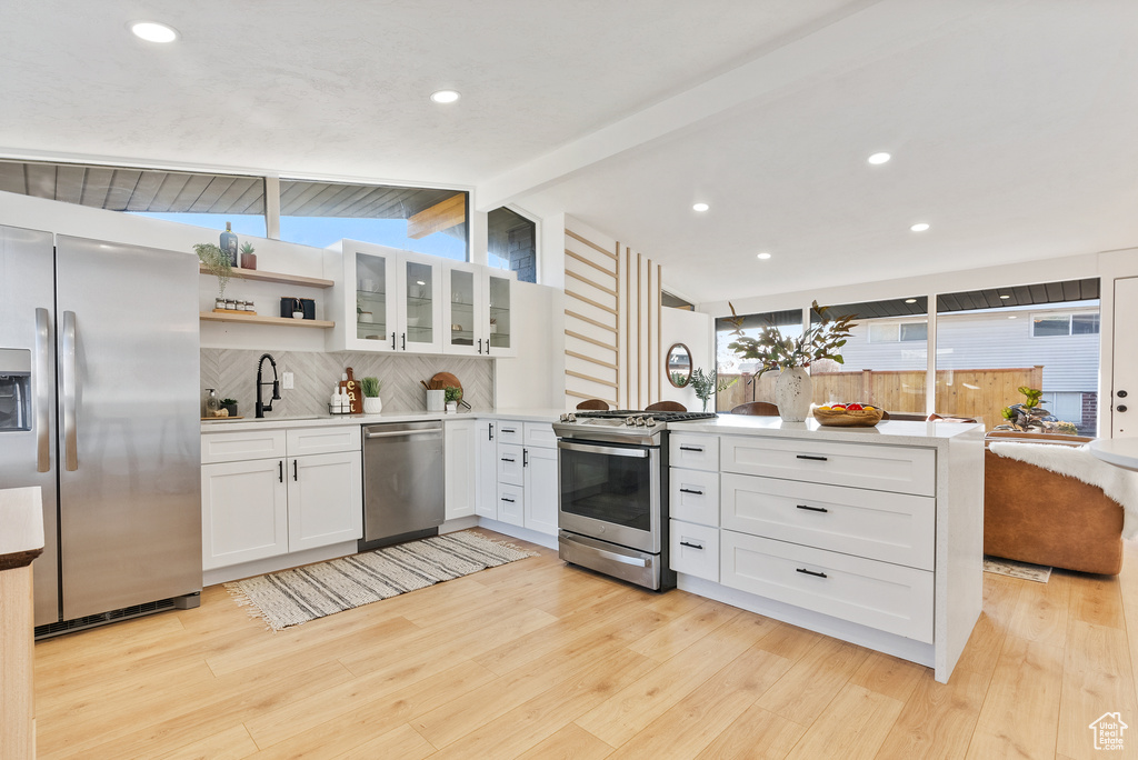 Kitchen with stainless steel appliances, a peninsula, a sink, decorative backsplash, and light wood finished floors