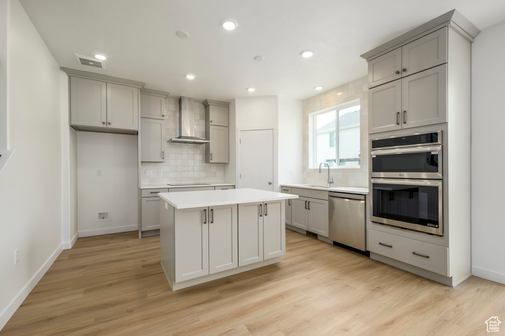 Kitchen featuring stainless steel appliances, wall chimney exhaust hood, gray cabinetry, and recessed lighting
