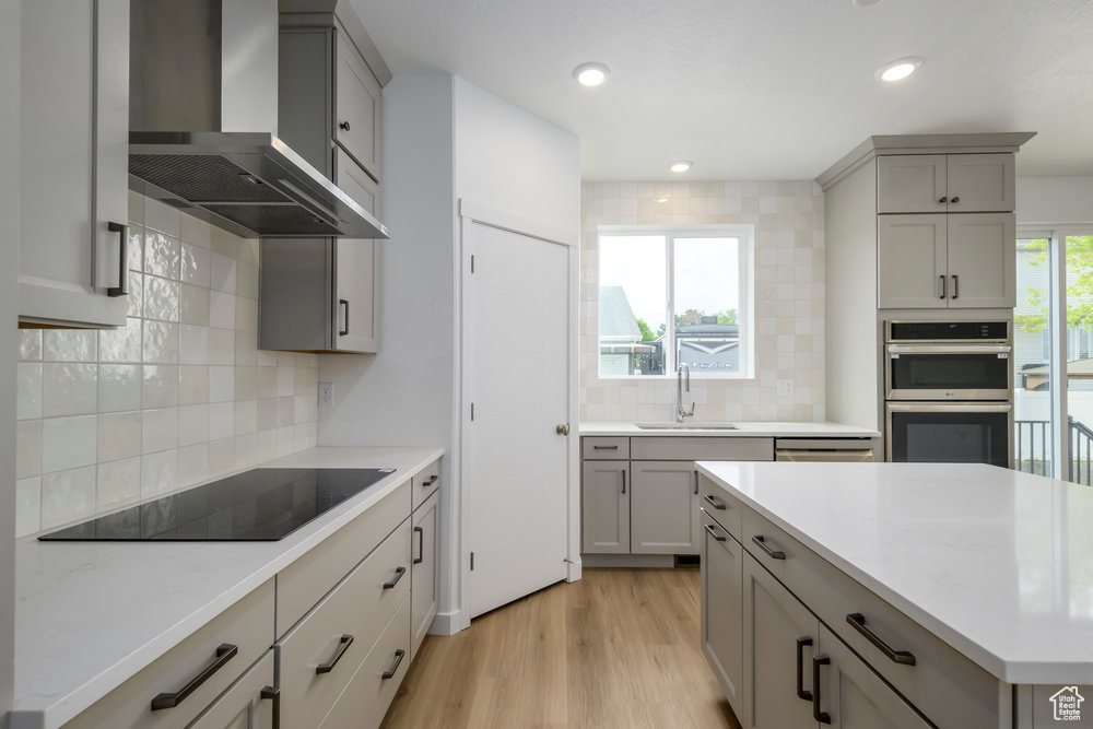 Kitchen featuring wall chimney exhaust hood, gray cabinetry, a sink, black electric cooktop, and backsplash