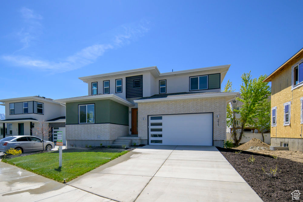 View of front facade with brick siding, an attached garage, driveway, stucco siding, and a front lawn