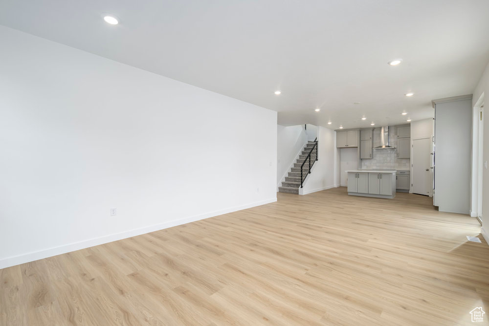 Unfurnished living room with recessed lighting, stairs, light wood finished floors, and baseboards