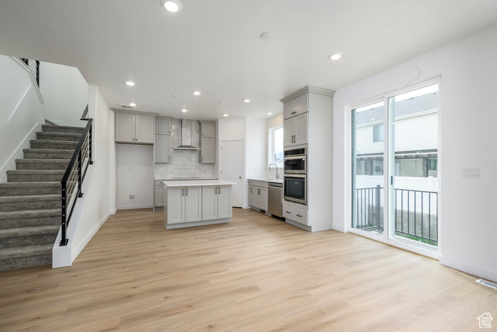 Kitchen featuring wall chimney range hood, gray cabinets, appliances with stainless steel finishes, a sink, and light wood finished floors