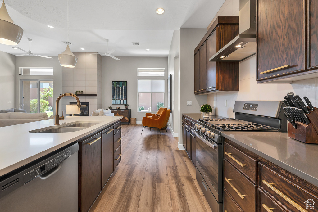 Kitchen featuring a sink, appliances with stainless steel finishes, ceiling fan, open floor plan, and wall chimney exhaust hood