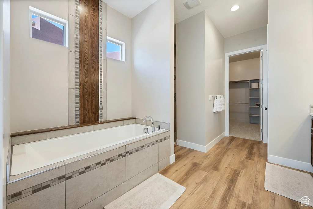 Full bath with a walk in closet, baseboards, wood finished floors, and a garden tub
