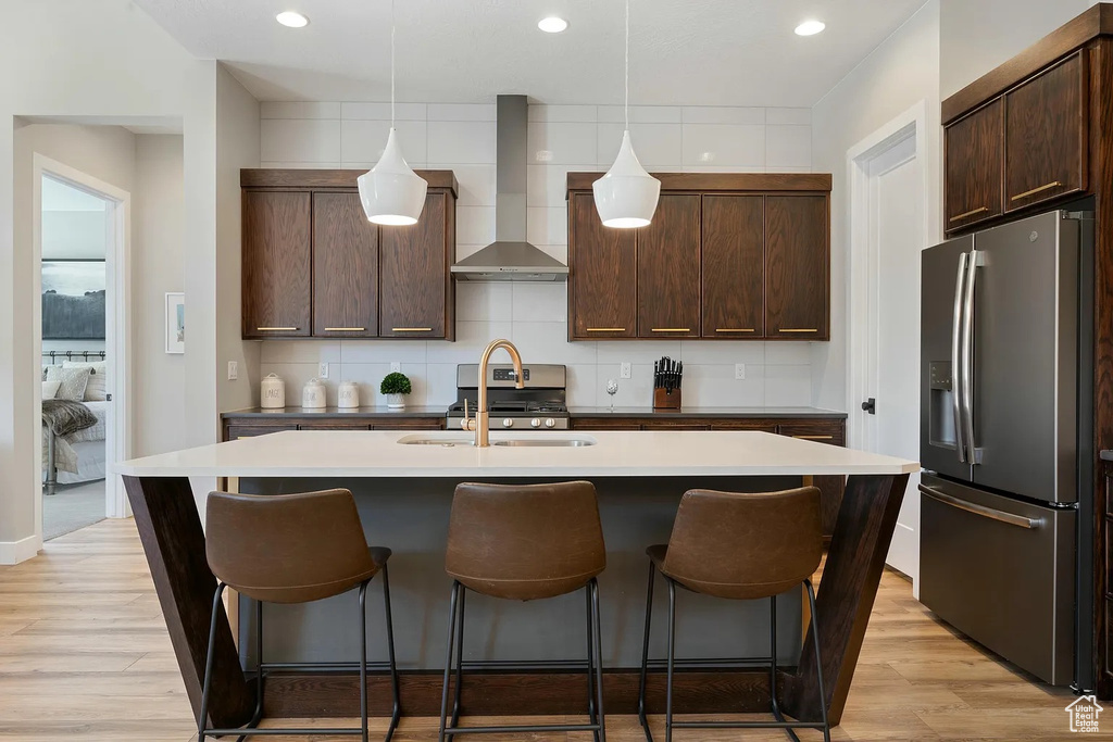 Kitchen featuring a breakfast bar area, stainless steel fridge, wall chimney range hood, and a sink