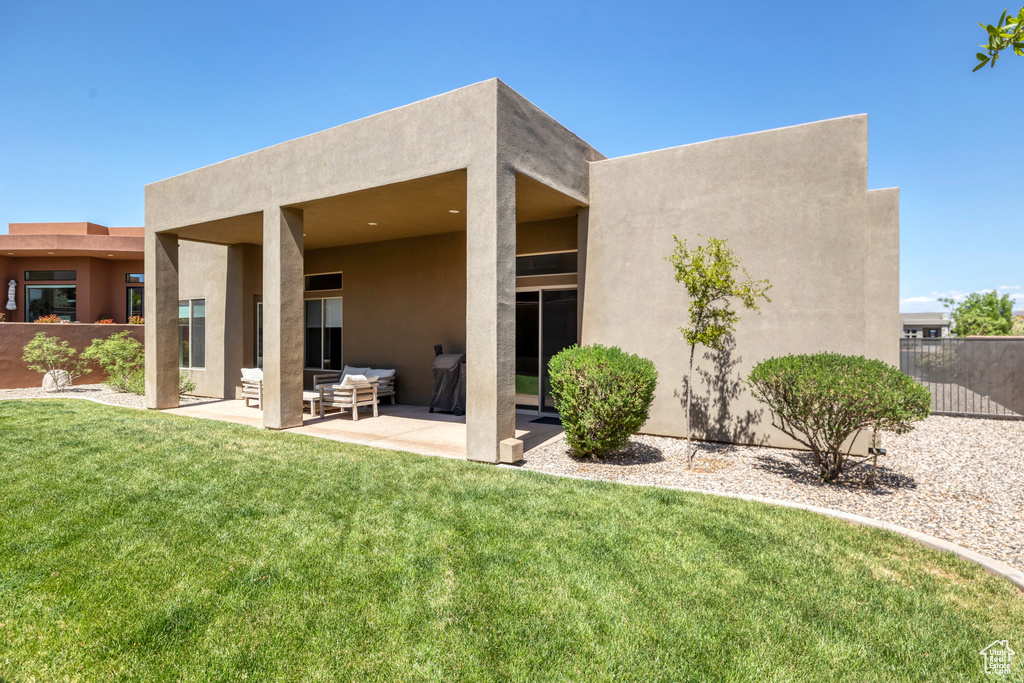 Rear view of property with stucco siding, fence, a lawn, and a patio