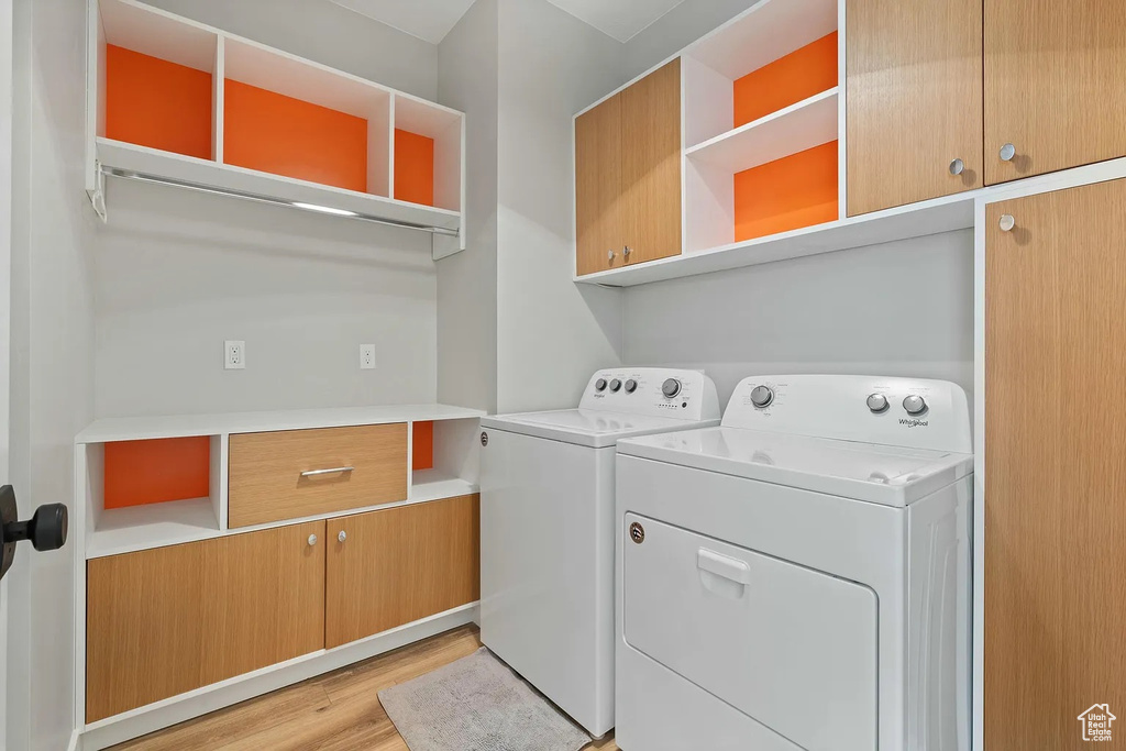 Washroom with light wood-type flooring, cabinet space, and washing machine and dryer