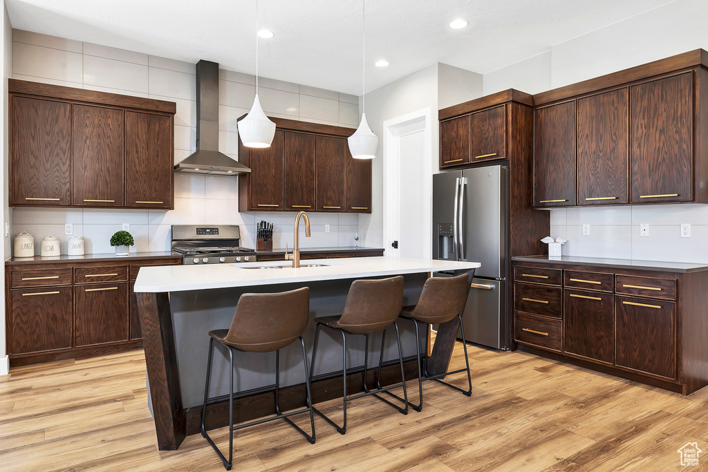Kitchen with a sink, stainless steel appliances, decorative backsplash, a kitchen bar, and wall chimney exhaust hood