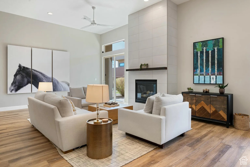 Living room featuring a tiled fireplace, ceiling fan, light wood-style flooring, baseboards, and a towering ceiling