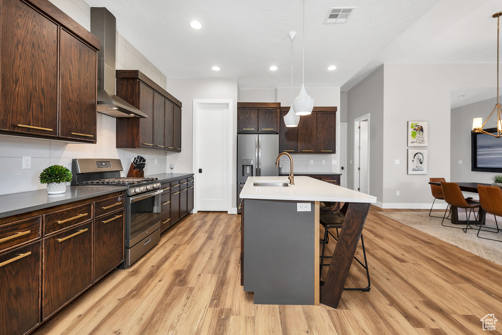 Kitchen featuring light wood-style flooring, visible vents, stainless steel appliances, baseboards, and wall chimney exhaust hood