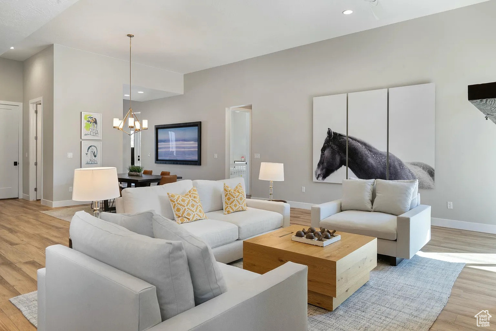Living room with light wood finished floors, recessed lighting, a notable chandelier, and baseboards