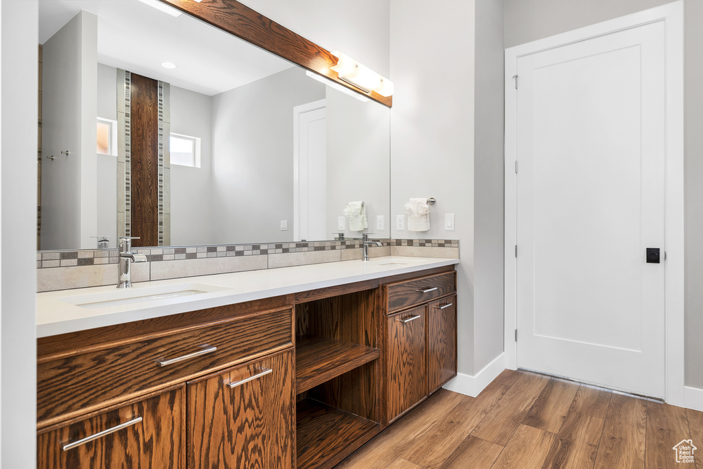 Bathroom featuring double vanity, a sink, wood finished floors, and decorative backsplash