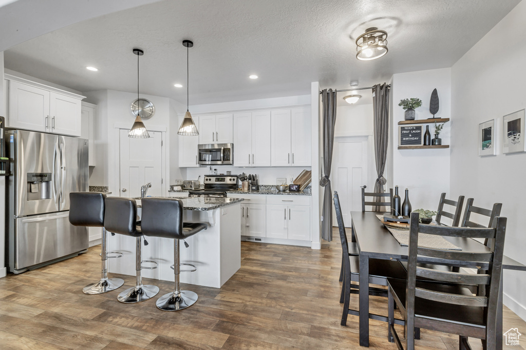 Kitchen featuring white cabinets, dark stone counters, a breakfast bar area, wood finished floors, and stainless steel appliances