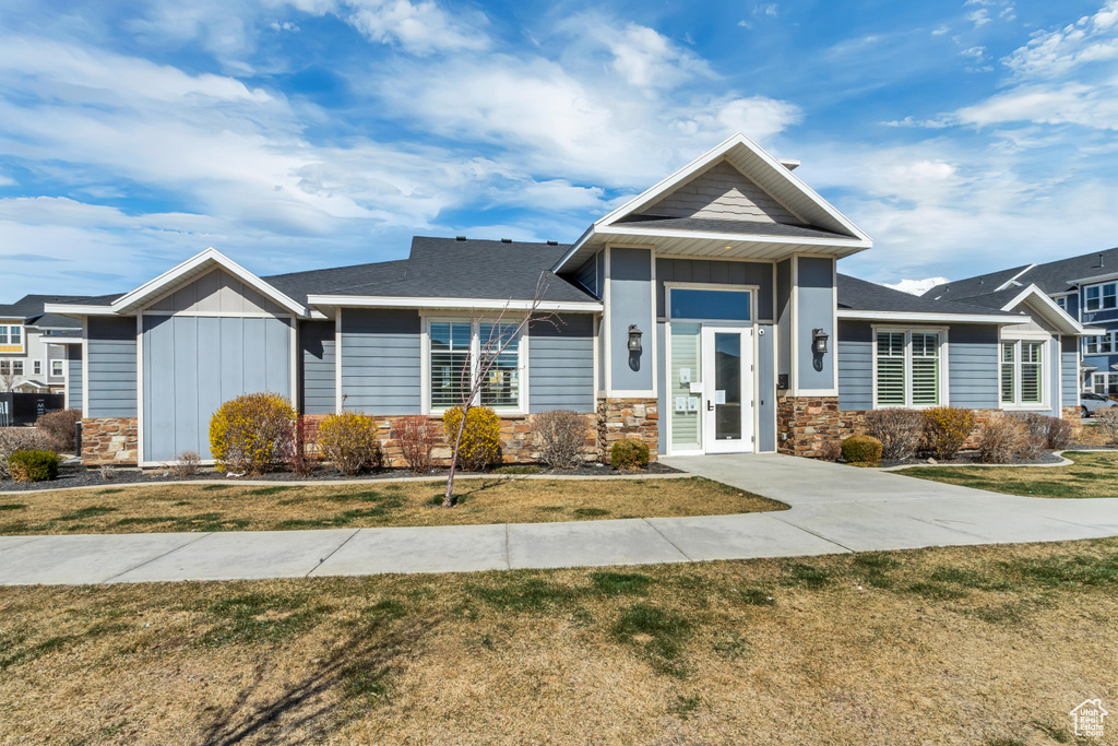 View of front facade featuring board and batten siding, stone siding, a shingled roof, and a front lawn