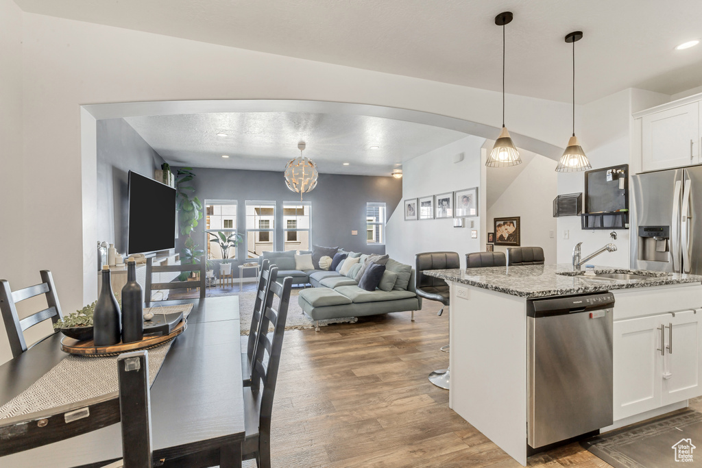 Kitchen featuring arched walkways, light stone counters, wood finished floors, a sink, and stainless steel dishwasher