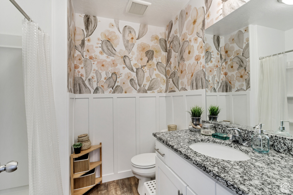 Bathroom with toilet, a decorative wall, vanity, visible vents, and wainscoting