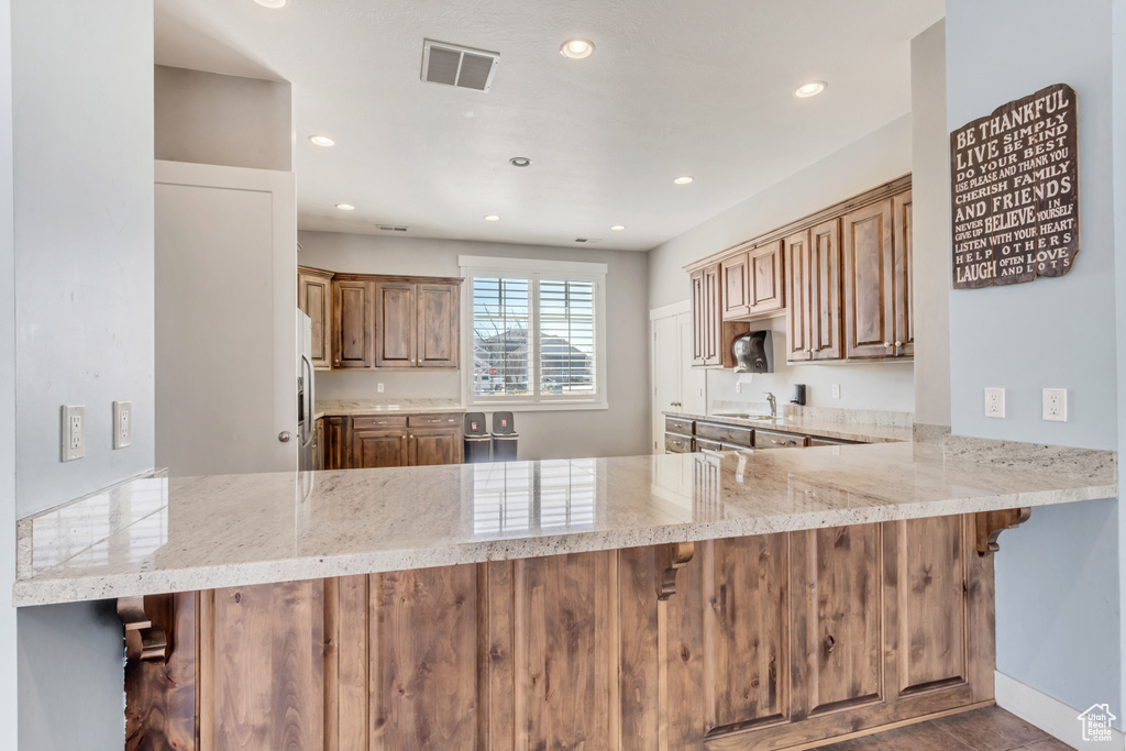 Kitchen featuring visible vents, a peninsula, light stone countertops, a sink, and recessed lighting