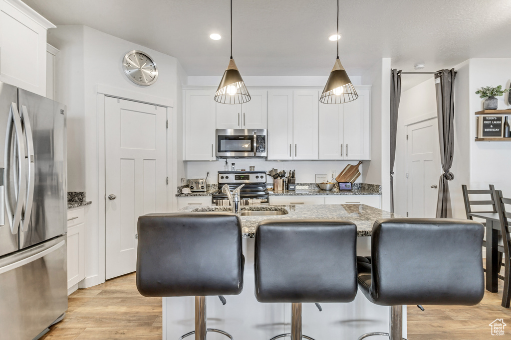 Kitchen with light wood finished floors, white cabinets, appliances with stainless steel finishes, a breakfast bar, and light stone countertops