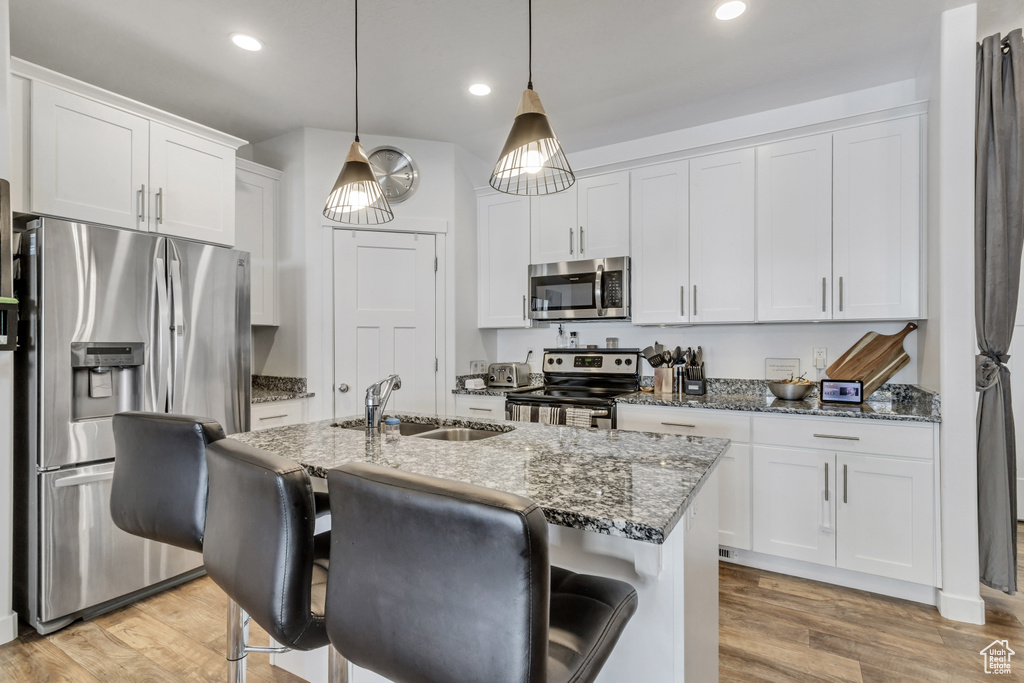 Kitchen featuring white cabinets, light wood-style flooring, dark stone countertops, stainless steel appliances, and a sink