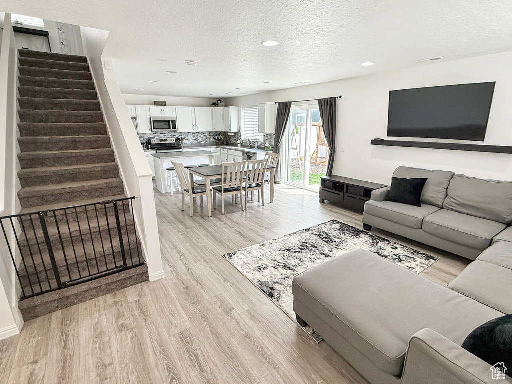 Living area with a textured ceiling, stairway, light wood finished floors, and recessed lighting