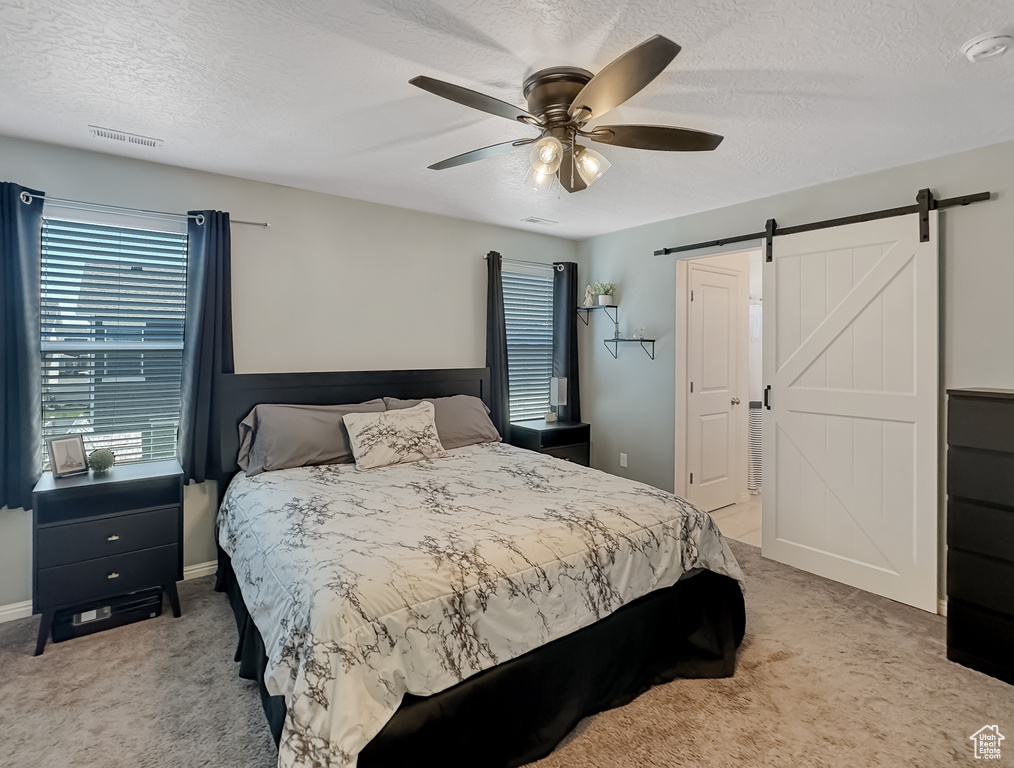 Bedroom featuring a textured ceiling, visible vents, ceiling fan, a barn door, and light carpet