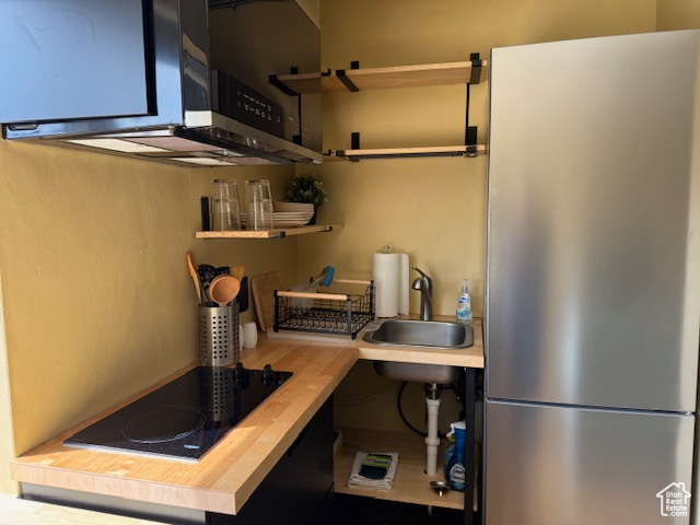 Kitchen featuring appliances with stainless steel finishes, a sink, butcher block counters, and open shelves