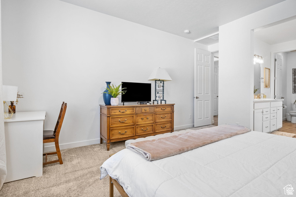 Bedroom featuring light colored carpet, a sink, baseboards, and ensuite bathroom