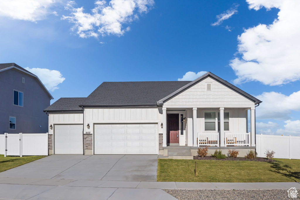 View of front of house with an attached garage, covered porch, fence, board and batten siding, and a front yard