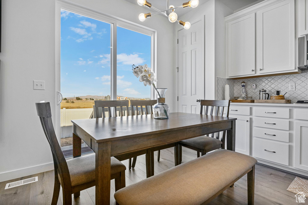 Dining room with visible vents, light wood-style flooring, baseboards, and an inviting chandelier