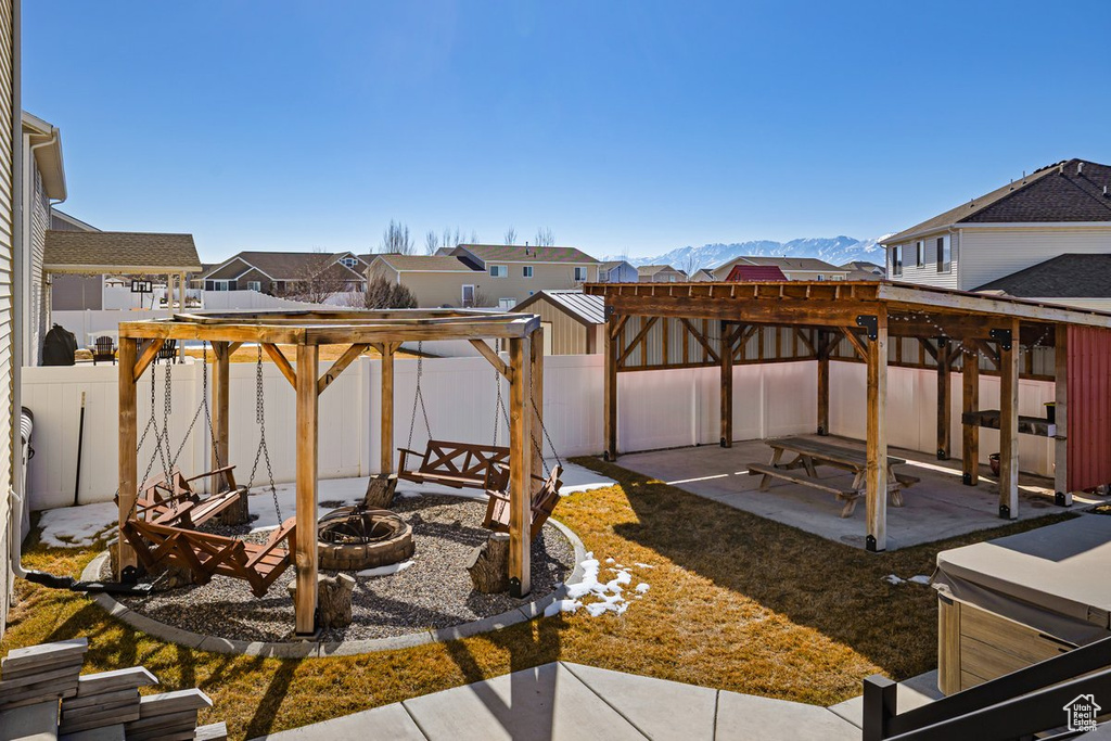 View of patio featuring a hot tub, a mountain view, a pergola, a fenced backyard, and a fire pit