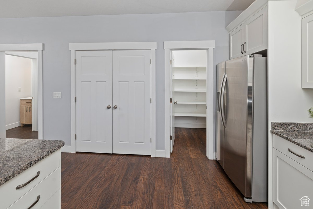 Kitchen featuring dark wood-type flooring, dark stone countertops, stainless steel fridge, and white cabinetry