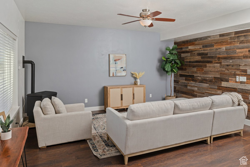 Living room with dark wood finished floors, a ceiling fan, an accent wall, a wood stove, and wooden walls