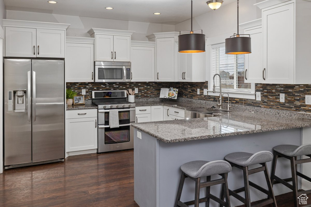 Kitchen with white cabinets, appliances with stainless steel finishes, a peninsula, light stone countertops, and a sink