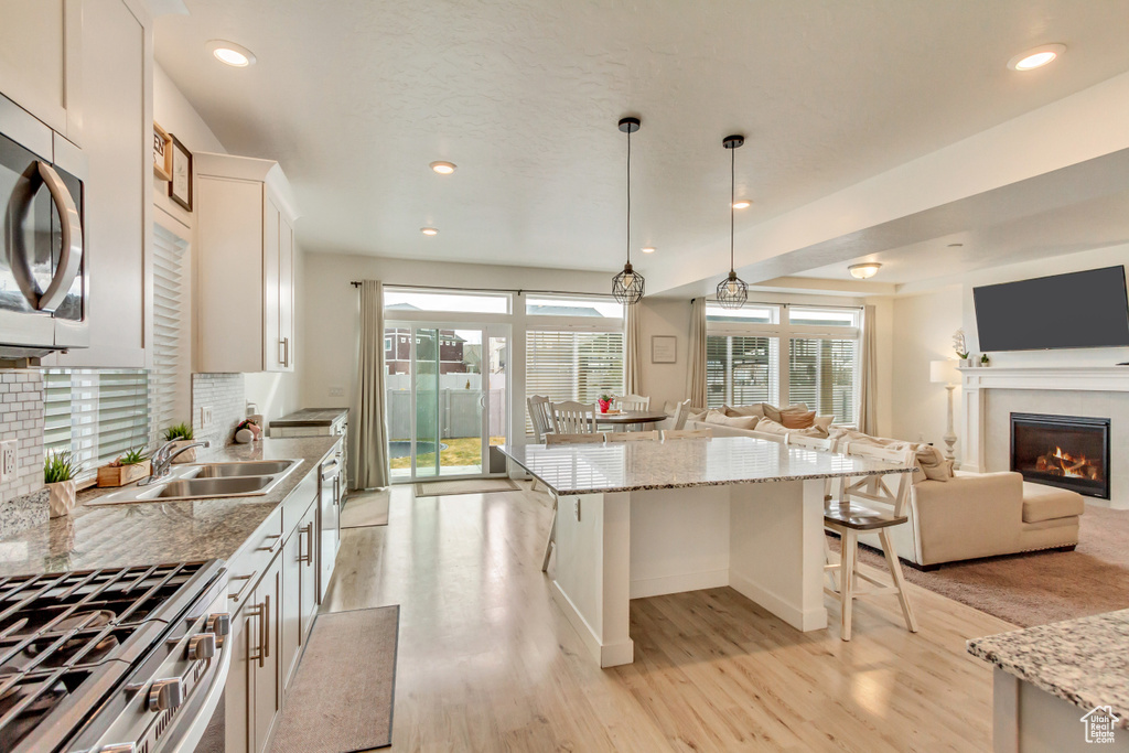 Kitchen featuring a warm lit fireplace, stainless steel microwave, open floor plan, a center island, and a sink