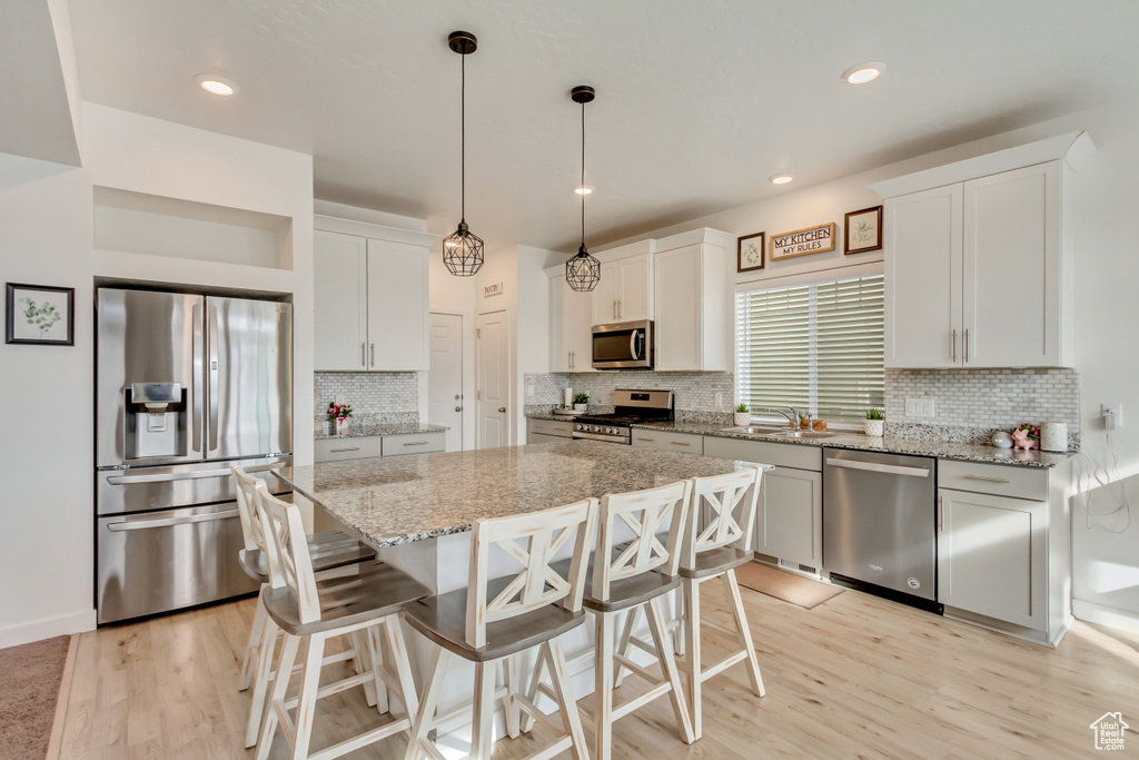 Kitchen with stainless steel appliances, a kitchen bar, light wood-style flooring, and a center island