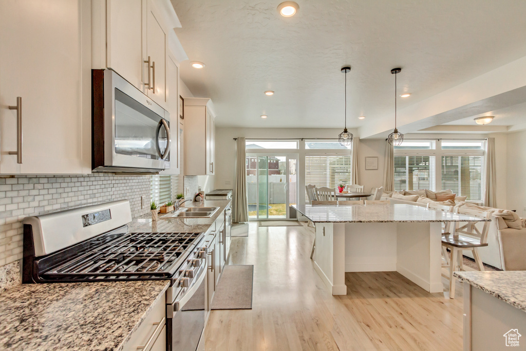 Kitchen featuring tasteful backsplash, a kitchen breakfast bar, open floor plan, stainless steel appliances, and light wood-style floors
