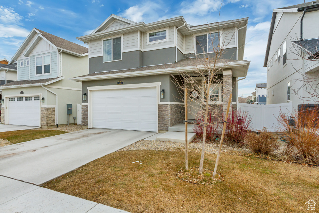 View of front of house featuring a garage, stone siding, fence, and driveway