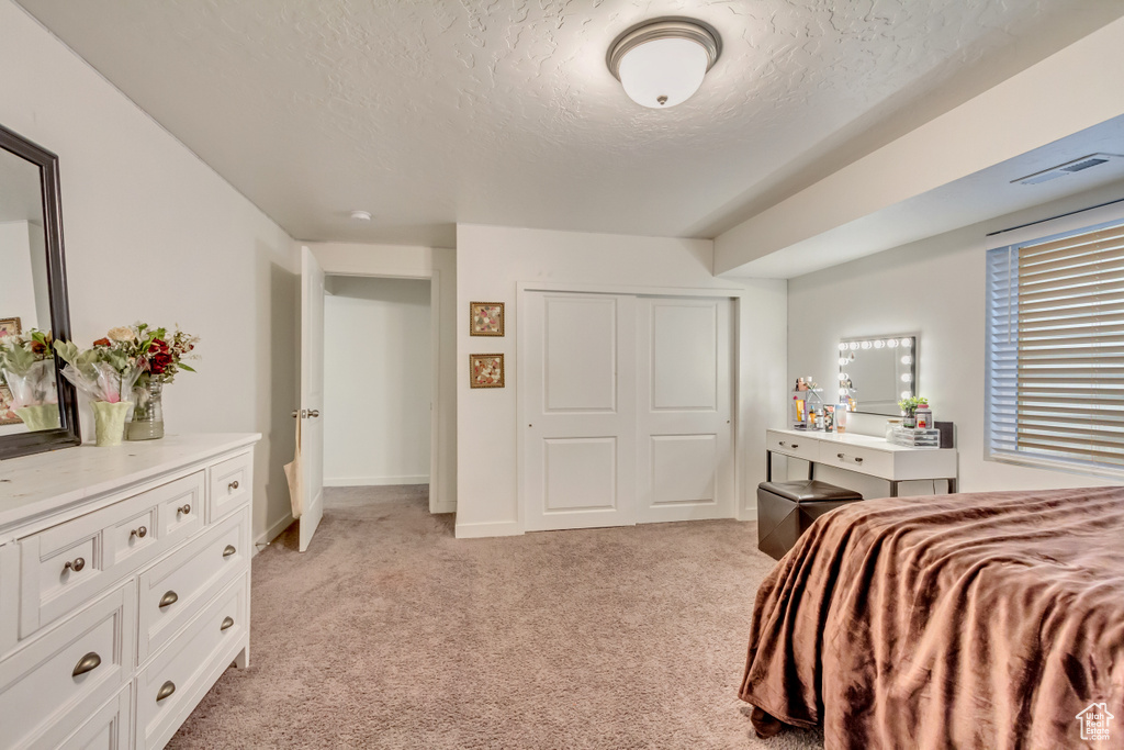 Bedroom featuring a closet, visible vents, light colored carpet, a textured ceiling, and baseboards